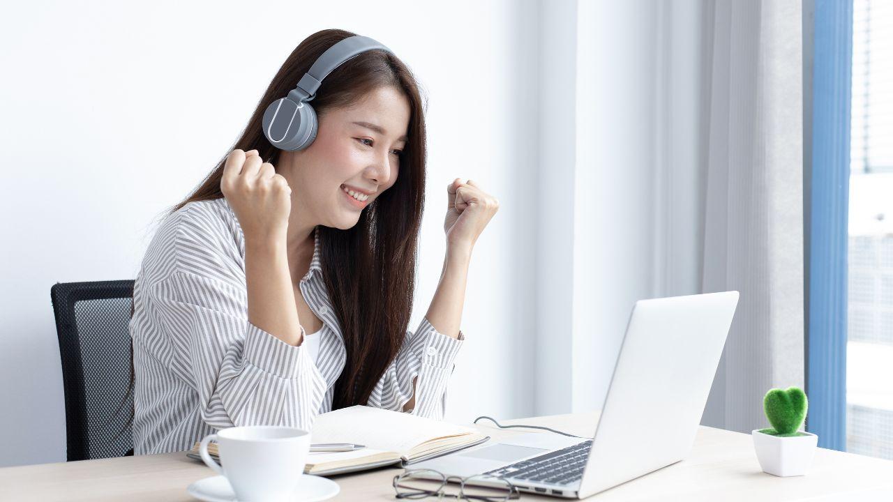 Una chica contenta mientras usa su portátil con auriculares
