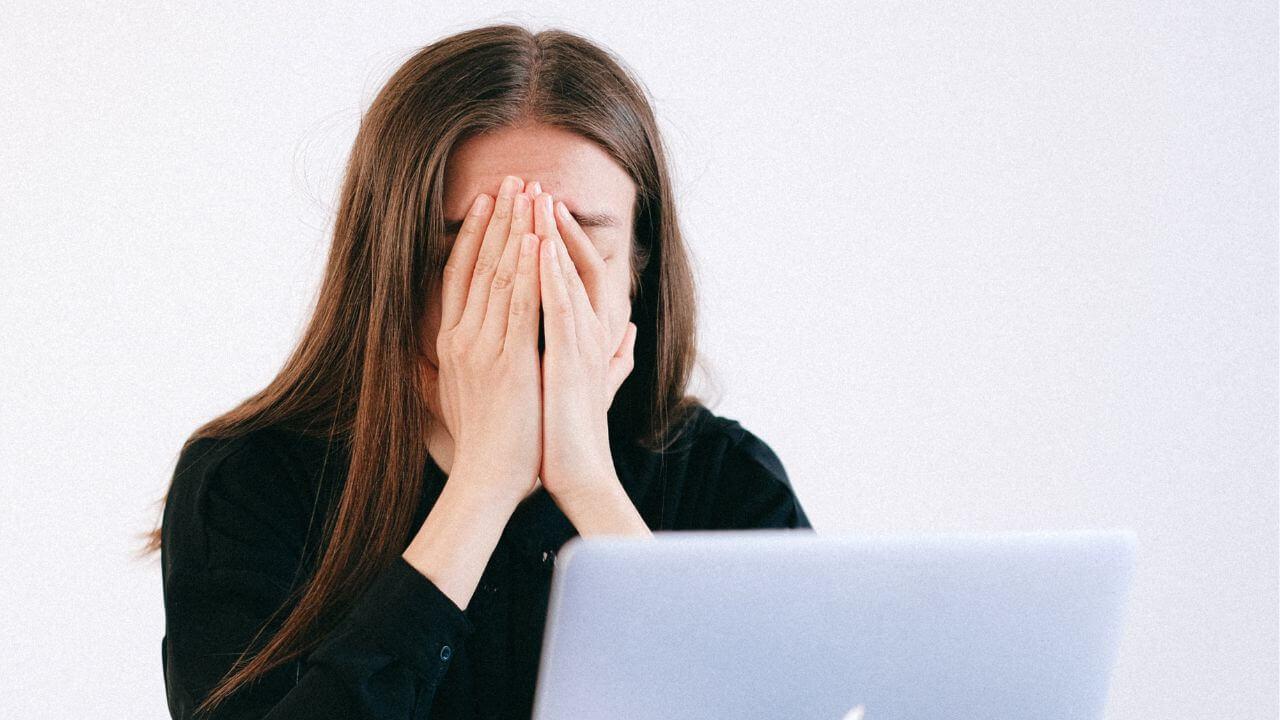 Una chica triste se lleva las manos a la cara delante del ordenador
