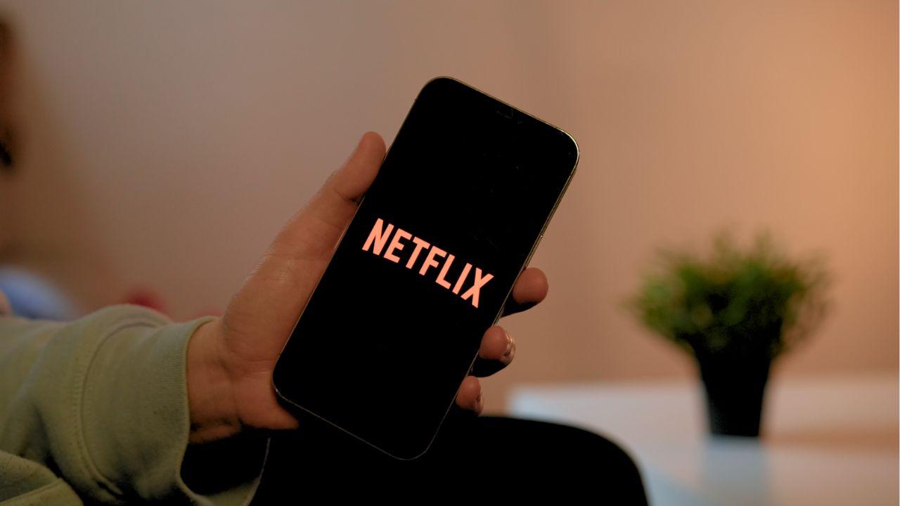 A man holds a cell phone with the Netflix logo on the screen