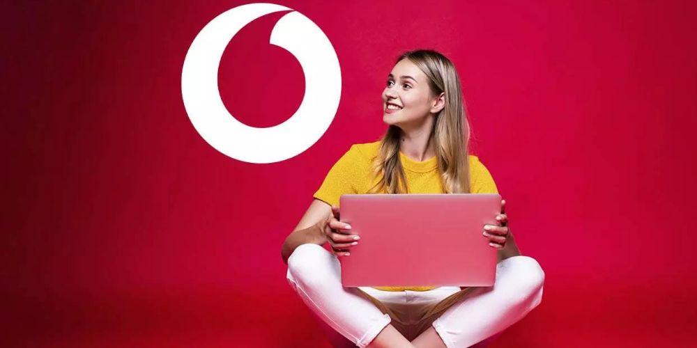 Una chica sentada con el portátil mirando al logo de Vodafone